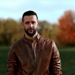 a man in a leather jacket standing in a field